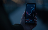 businessman-trader-using-mobile-phone-check-real-time-stock-market-data-while-standing-outdoors-selective-focus-male-hand-holding-smartphone-with-forex-graph-chart 1